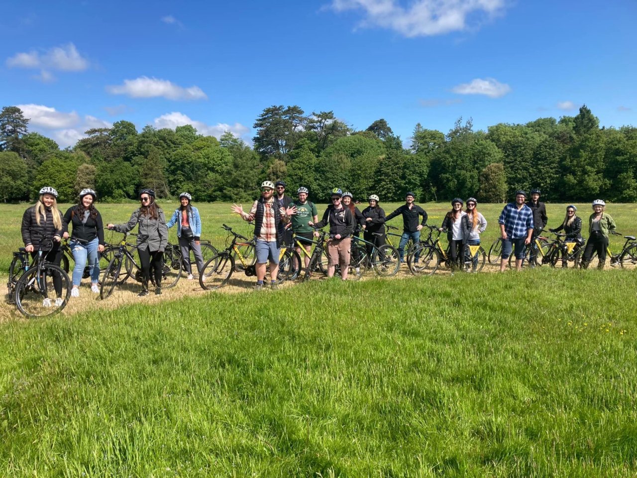 large group of people on bikes beside grass on dirt path 